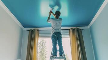 un hombre soportes en un escalera meticulosamente pintura el techo de su dormitorio en un negrita y juguetón color dando el habitación un único y personalizado toque foto