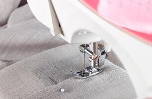 Modern sewing machine presser foot with linen fabric and thread, closeup photo