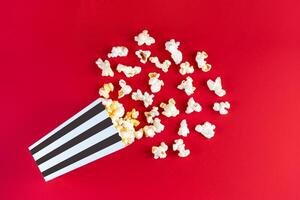 Tasty cheese popcorn falling out of a black striped carton bucket, isolated on red background photo