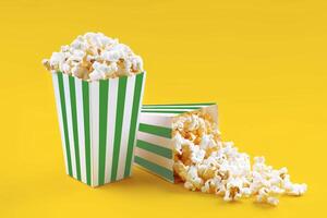 Two green white striped carton buckets with tasty cheese popcorn, isolated on yellow background photo