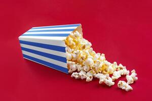 Tasty cheese popcorn falling out of a blue striped carton bucket, isolated on red background photo