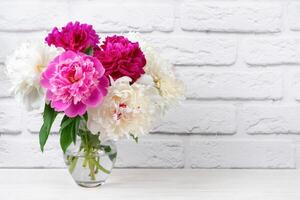 Bouquet of pink and white peony flowers in vase on white brick wall background photo