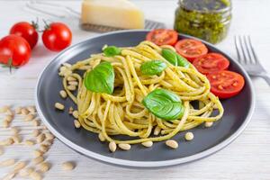 tradicional italiano espaguetis pasta pesto con Fresco albahaca hojas y ingredientes en negro plato foto