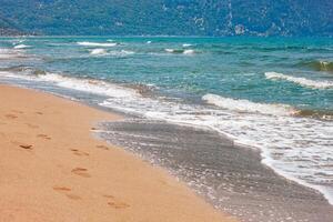 Blue and turquoise color sea waves with white foam and yellow sandy beach photo