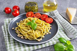tradicional italiano espaguetis pasta pesto con Fresco albahaca hojas y ingredientes en gris antecedentes foto