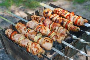 Grilled pieces of meat on skewers, shish kebab with vegetables, cooking process on brazier photo