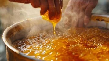 A hand stirring a large pot of freshly harvested honey with steam rising from its sticky surface photo