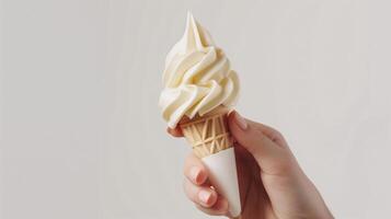 Hand Presenting a Classic Scooped Vanilla Ice Cream Cone on a Plain Backdrop photo