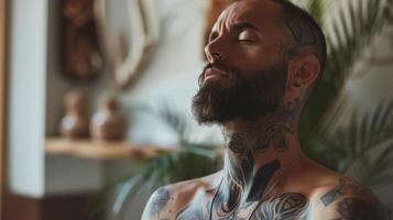 un hombre con tatuajes y un barba respiración profundamente y despacio como él sostiene un restaurativo yoga actitud hallazgo interior paz y emocional equilibrar foto