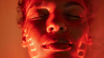 A closeup of a persons face illuminated by the faint red glow of an infrared sauna. They seem blissfully relaxed and at peace perhaps having just finished a calming meditation session photo