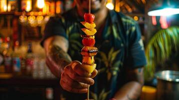 A mixologist carefully holds a bamboo skewer of assorted exotic fruits which will be used as a garnish for a rum and banana liqueur drink photo