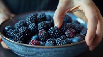 A persons hand reaching towards a bowl of small round fruits with a glossy purple skin and delicate white photo