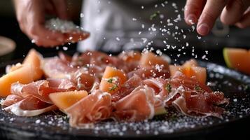 A person sprinkling sea salt flakes over a platter of thinly sliced prosciutto and melon photo