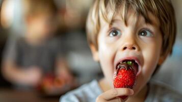 un joven chico sostiene un chocolate sumergido fresa su ojos ensanchamiento en sorpresa como él sabores el inesperado Estallar de sabor desde el chocolate revestimiento foto