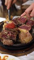 Process of cutting the medium rare steak with vegetables on a cutting board. The juicy beef meat is cut into pieces with fork and knife. Gourmet menu at restaurant. Unrecognizable person eat beef video