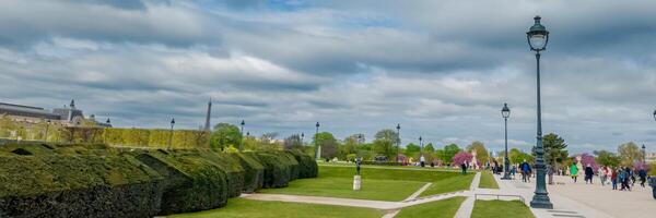 Panoramic view of a bustling urban park in springtime, featuring lush greenery and people enjoying a leisurely walk, with an iconic tower in the background photo