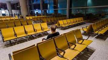 Lone traveler sitting in an empty airport waiting area with rows of yellow seats, suggesting travel, business trips, or holiday commuting photo