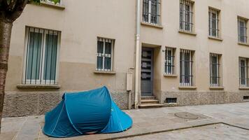 A blue tent pitched on an urban sidewalk next to a beige building, symbolizing issues like homelessness and urban camping photo