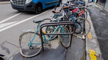 Urban bicycle parking with various bikes secured to metal racks on a city street, with a blue van passing by, depicting eco friendly transportation photo