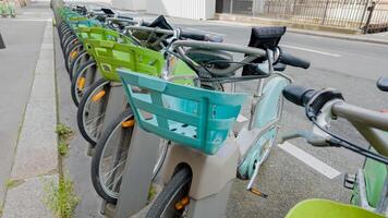 Row of public rental bicycles with baskets parked at a bike sharing station on an urban street, representing eco friendly transportation and sustainable travel photo