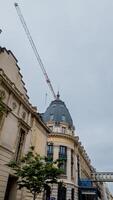 Construction crane towering over a European classical architecture building under a cloudy sky, implying urban development and architectural preservation photo