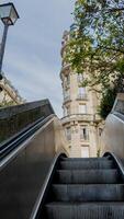 Emerging from a subway station, the escalator leads to a classic European style building against a clear sky, hinting at urban exploration or daily commute photo