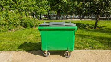 Bright green waste container in a sunlit urban park setting, symbolizing environmental conservation and cleanliness, suitable for Earth Day and public service campaigns photo