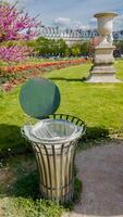 Public garden trashcan with a swinging lid amidst blooming spring flowers, symbolizing urban cleanliness and environmental conservation efforts photo