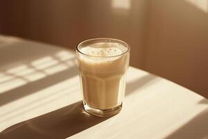 Glass of frothy milk on a table, soft light casting a shadow against a beige to white gradient background photo