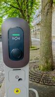 Modern electric vehicle charging station on a city street with lush green trees, signifying sustainable transportation and environmental awareness photo