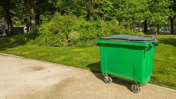 Large green waste container in a lush park on a sunny day, symbolizing environmental sustainability and waste management practices photo