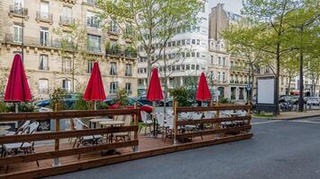 Quaint European street side cafe with closed red umbrellas, ideal for concepts related to urban dining, travel, or springtime leisure photo