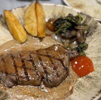 Sirloin steak grilled medium rare served with potatoes and salad with mushroom black pepper sauce in a restaurant photo