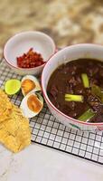 Rawon or Indonesian black beef soup, black color are from indonesian nut called kluwek. Served with lime, chili paste, salted egg, and tempe cracker. Perfect for recipe, article, or any cooking photo