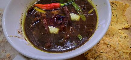 Rawon or Indonesian black beef soup, black color are from indonesian nut called kluwek. Served with lime, chili paste, salted egg, and tempe cracker. Perfect for recipe, article, or any cooking photo