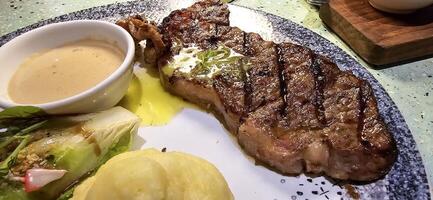 Beef New York strip loin steak or sirloin steak served with potatoes, and mushroom sauce and salad on plate photo
