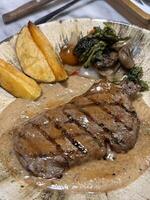 Sirloin steak grilled medium rare served with potatoes and salad with mushroom black pepper sauce in a restaurant photo