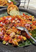 Spicy condiment of Indonesian sambal dabu dabu made of chilli, tomato and shallot with lemon basil in a ceramic bowl, wooden spoon on grey background photo