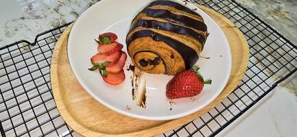 Fresh homemade striped chocolate croissant with chocolate filling on a round white plate, served with fresh strawberry photo