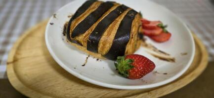 Fresh homemade striped chocolate croissant with chocolate filling on a round white plate, served with fresh strawberry photo