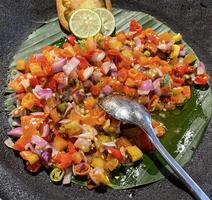 picante condimento de indonesio sambal Dabú Dabú hecho de chile, tomate y chalote con limón albahaca en un cerámico bol, de madera cuchara en gris antecedentes foto