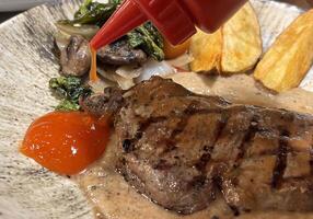 Sirloin steak grilled medium rare served with potatoes and salad with mushroom black pepper sauce in a restaurant photo