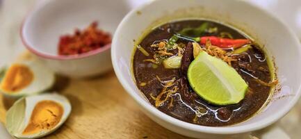 Rawon or Indonesian black beef soup, black color are from indonesian nut called kluwek. Served with lime, chili paste, salted egg, and tempe cracker. Perfect for recipe, article, or any cooking photo