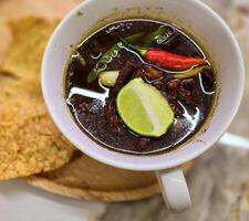 Rawon or Indonesian black beef soup, black color are from indonesian nut called kluwek. Served with lime, chili paste, salted egg, and tempe cracker. Perfect for recipe, article, or any cooking photo