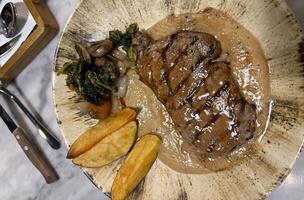 Sirloin steak grilled medium rare served with potatoes and salad with mushroom black pepper sauce in a restaurant photo