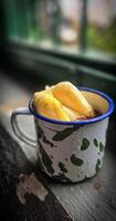 Ice chocolate drink on a vintage Indonesian iron mug with random green pattern called Blirik cup or cangkir Blirik on bokeh background along with chocolate filling bread photo