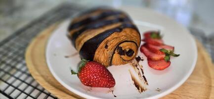 Fresh homemade striped chocolate croissant with chocolate filling on a round white plate, served with fresh strawberry photo