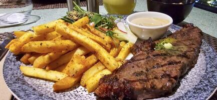 Beef New York strip loin steak or sirloin steak served with potatoes, and mushroom sauce and salad on plate photo