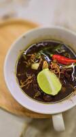 Rawon or Indonesian black beef soup, black color are from indonesian nut called kluwek. Served with lime, chili paste, salted egg, and tempe cracker. Perfect for recipe, article, or any cooking photo