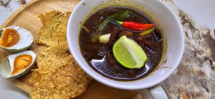 Rawon or Indonesian black beef soup, black color are from indonesian nut called kluwek. Served with lime, chili paste, salted egg, and tempe cracker. Perfect for recipe, article, or any cooking photo